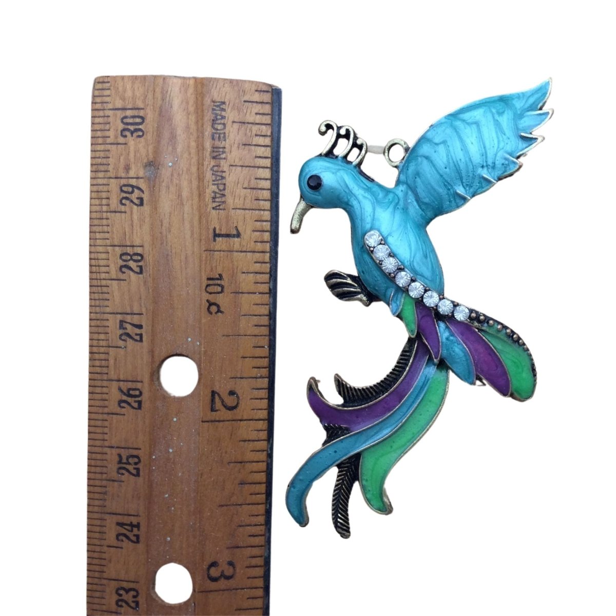 colorful bird pendant with crystal jewels next to a ruler for sizing. 