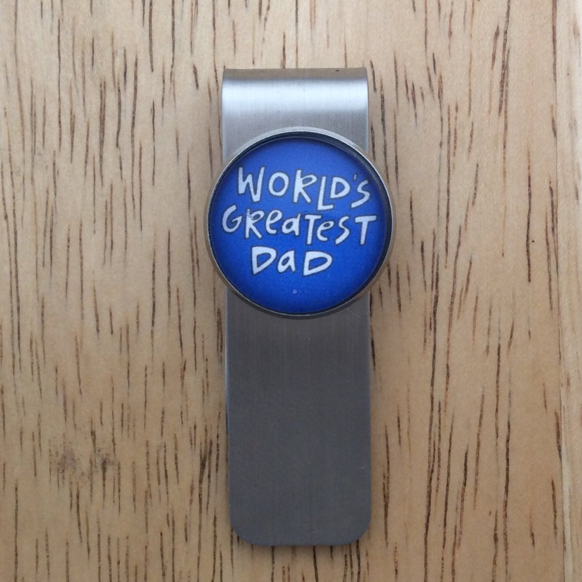 Stainless steel money clip with a blue cabochon setting that says " worlds greatest dad"