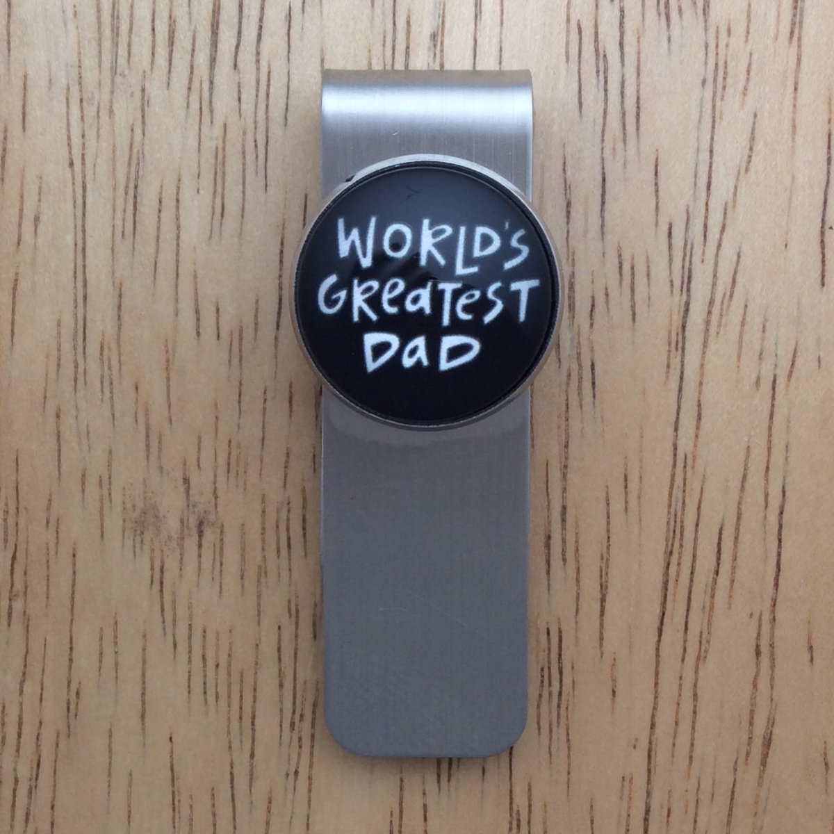 Stainless steel money clip with a black cabochon setting that says " world greatest dad"