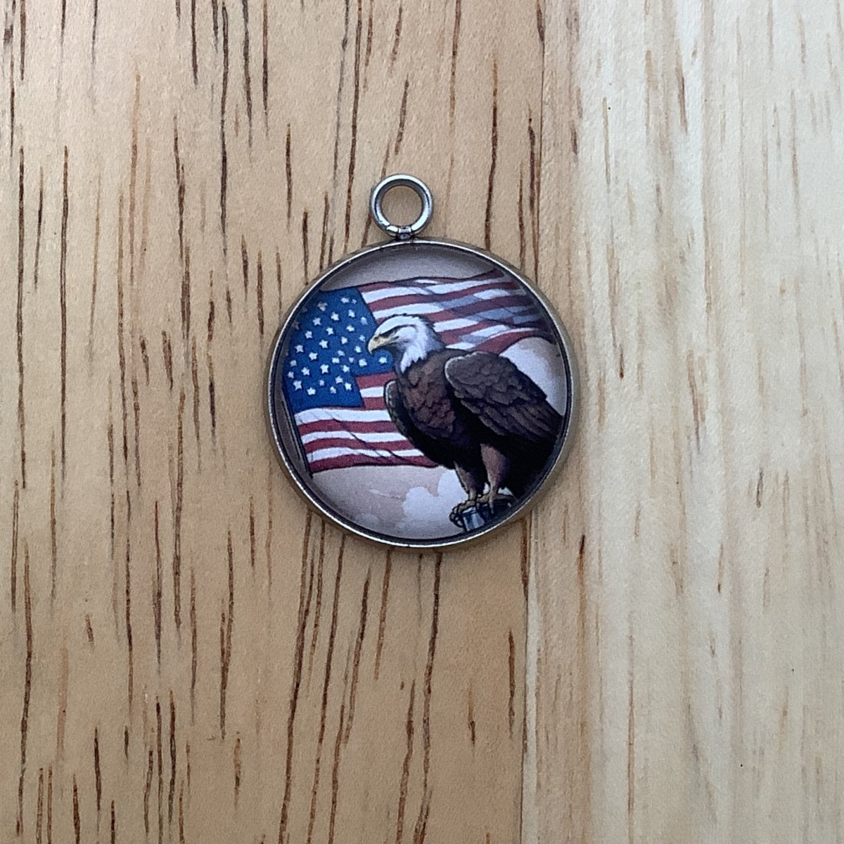 charm of a bald eagle standing magestically atop a flagpole with an American Flag in the backgroud