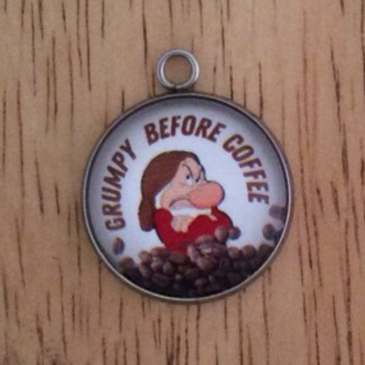 glass cabochon charm with grumpy behind a pile of coffee beans and it says Grumpy Before Coffee