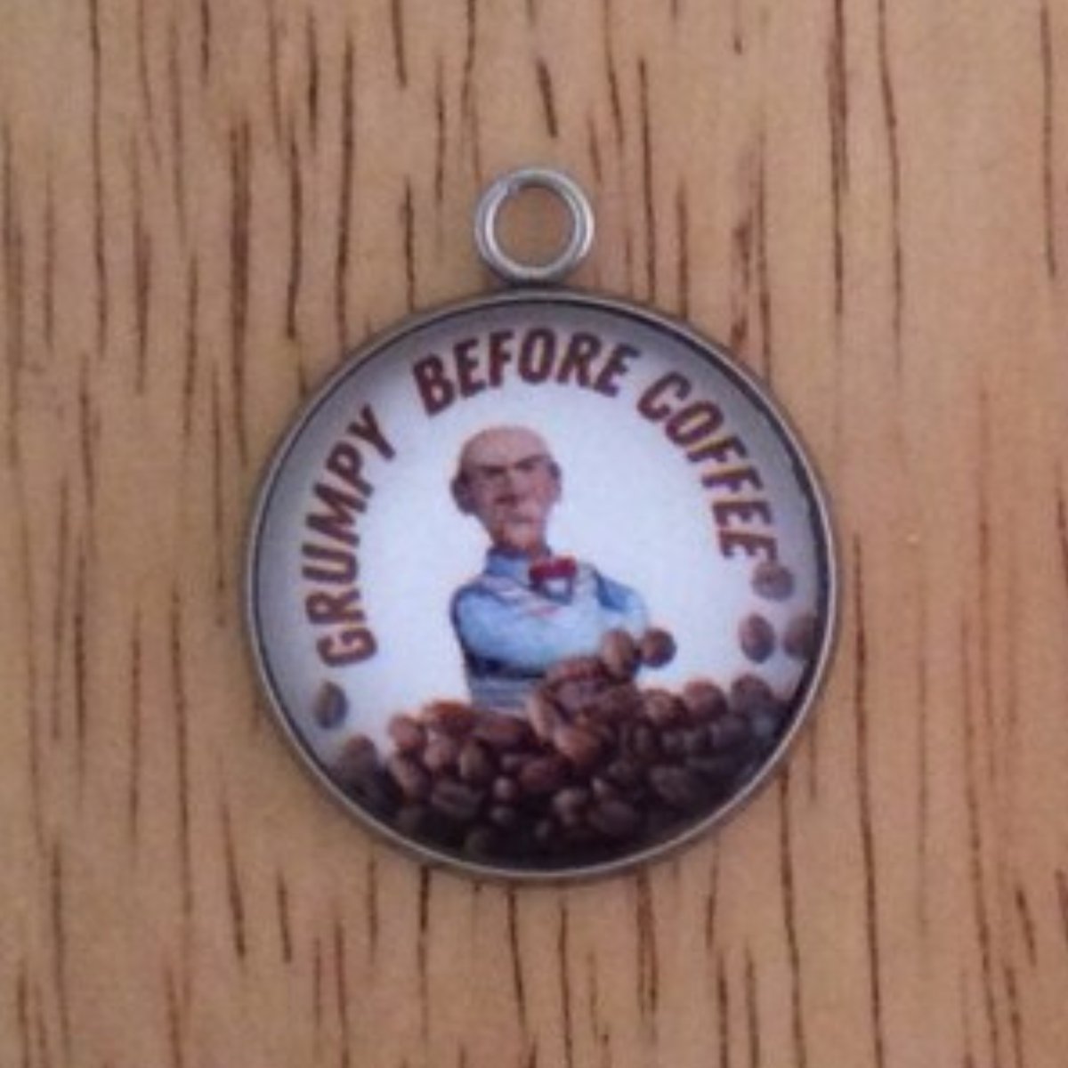 glass cabochon charm with a grumpy old man behind a pile of coffee beans and it says Grumpy Before Coffee