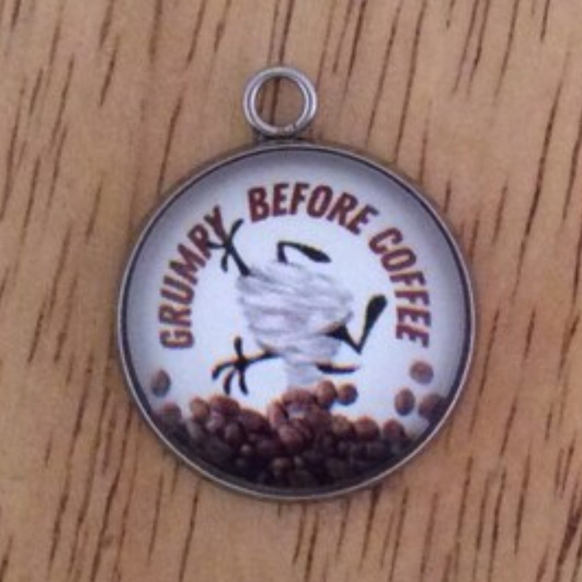 glass cabochon charm with a Tasmanian tornado behind a pile of co beans and it says Grumpy Before Coffee