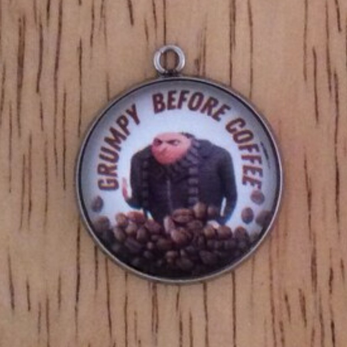 glass cabochon charm with  Gru behind a pile of coffee beans and it says Grumpy Before Coffee