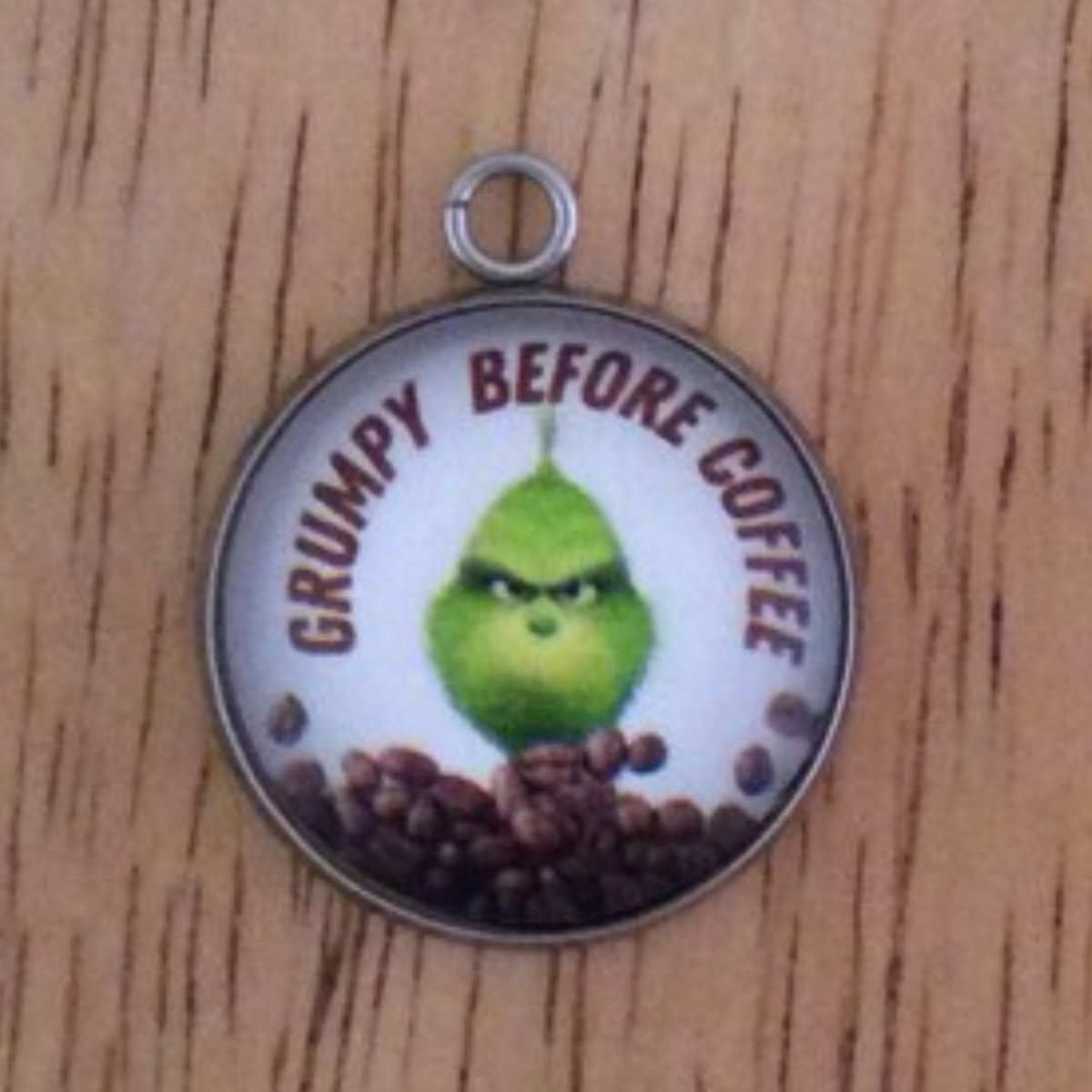 glass cabochon charm with a grinch behind a pile of coffee beans and it says Grumpy Before Coffee