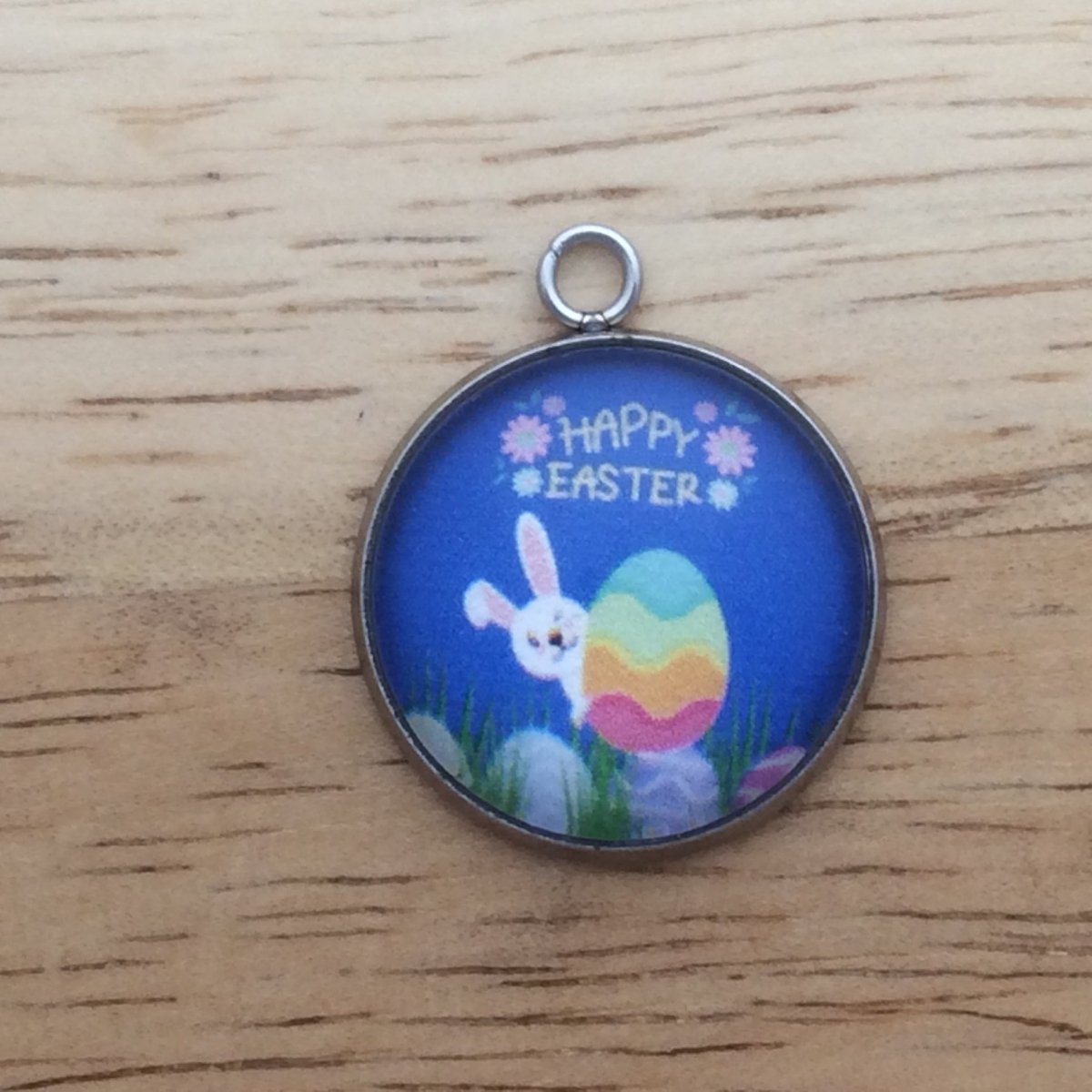 glass cabochon charm with a bunny peeking out from behind an easter egg and it says happy easter.