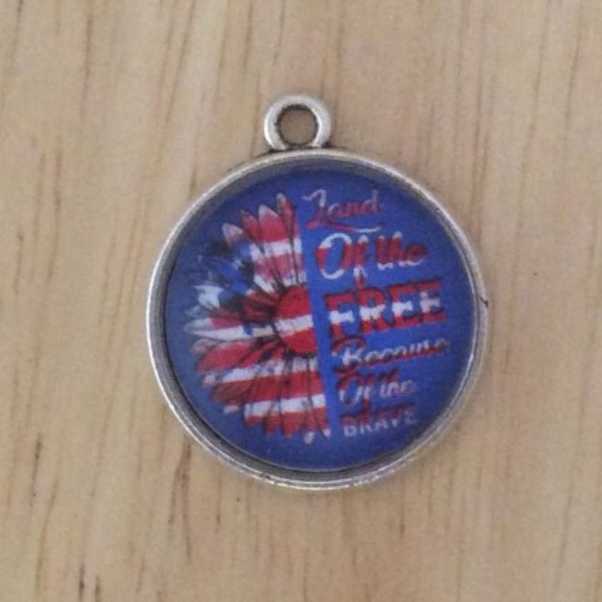 glass cabochon charm with an American flag sunflower that says land of the free because of the brave