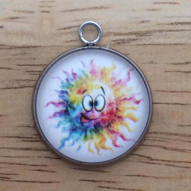 Glass cabochon charm with a funny faced, rainbow colored sun