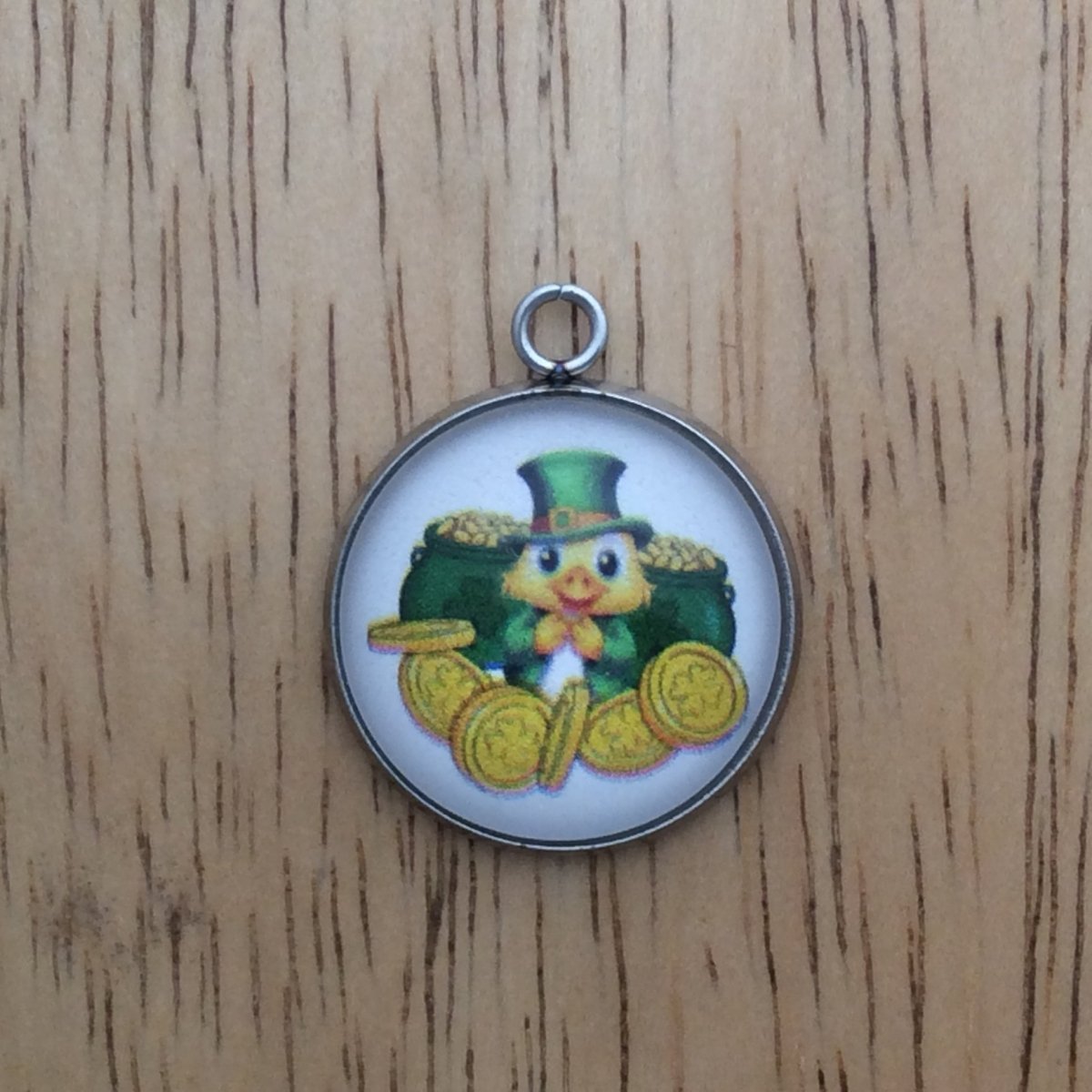 glass cabochon charm with a duct in front of two pots of gold with gold coins in front