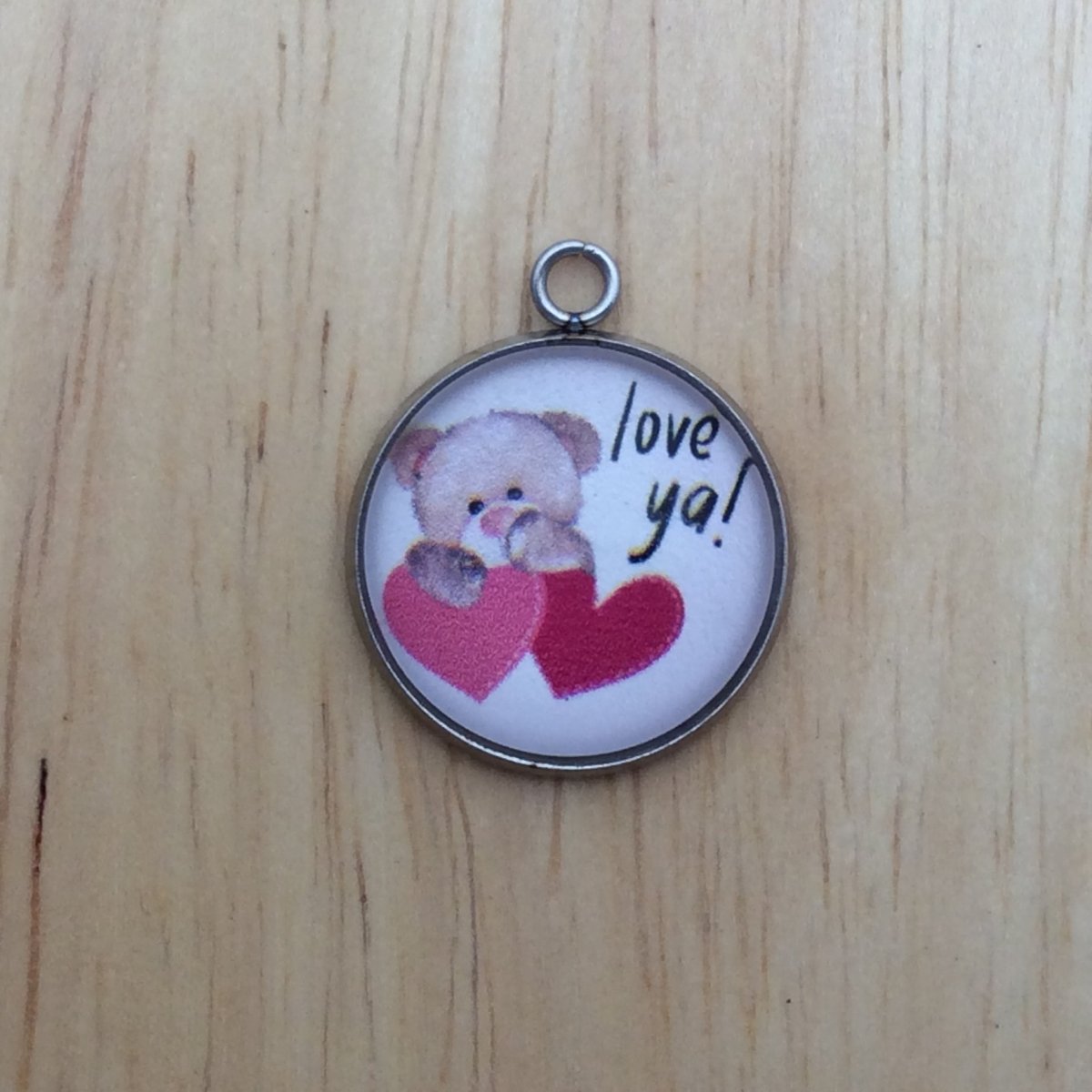 one glass cabochon charm that has a teddy bear with one pink heart and one red heart with the phrase Love Ya!