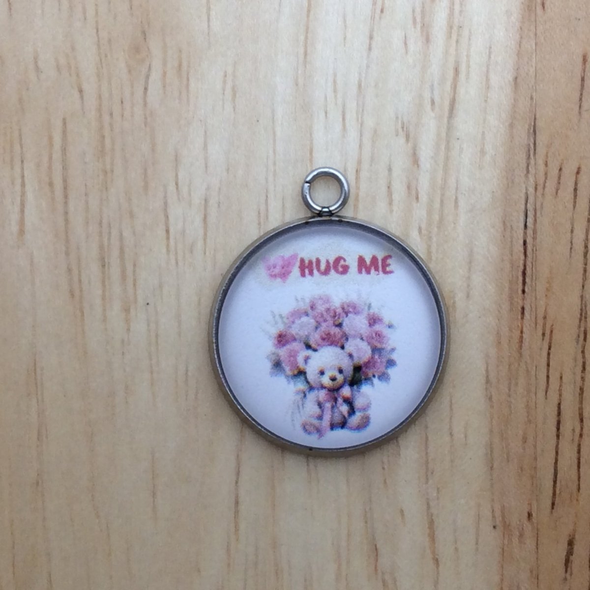 One glass cabochon charm that says Hug Me with a bouquet of pink and red roses with a teddy bear sitting in front