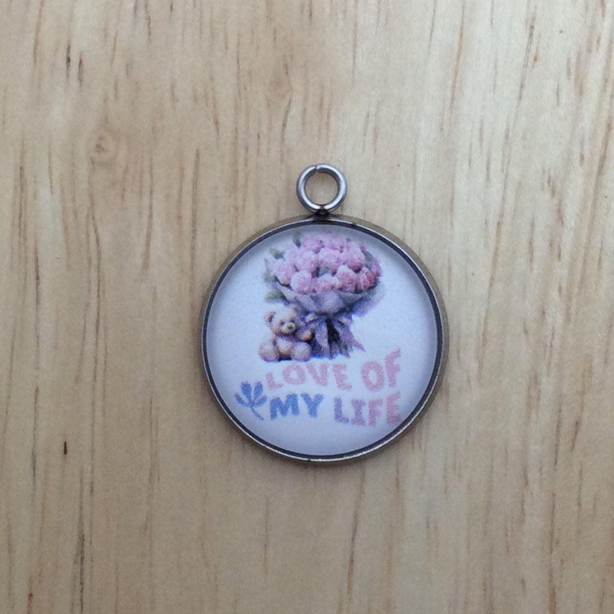 One glass cabochon charm with a small teddy bear beside a bouquet of pink roses and it says Love of my life