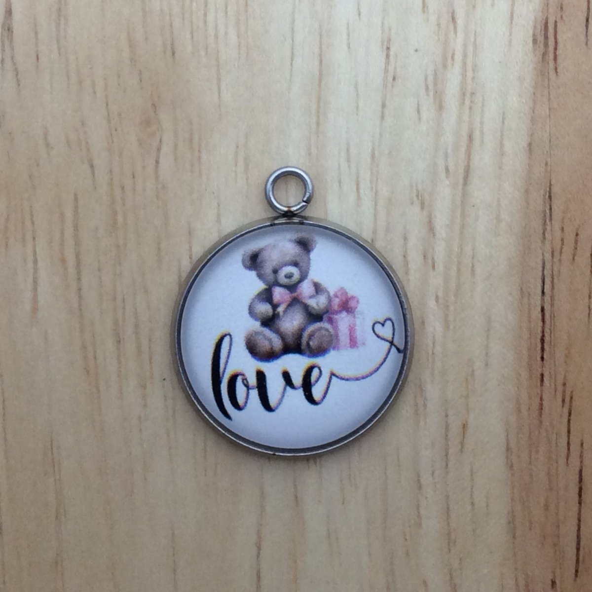 one glass cabochon charm with a teddy bear sitting with a present over the word LOVE