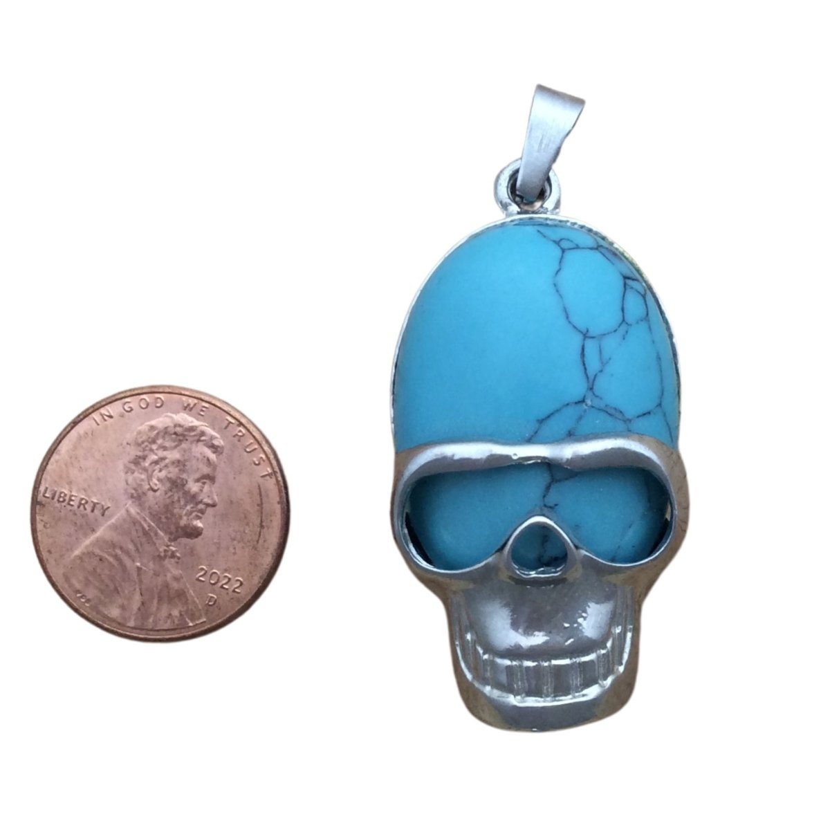 Turquoise stone with a Tibetan silver skull face mask pendant, next to a penny for sizing. pendant is  1 3/4" X 1"