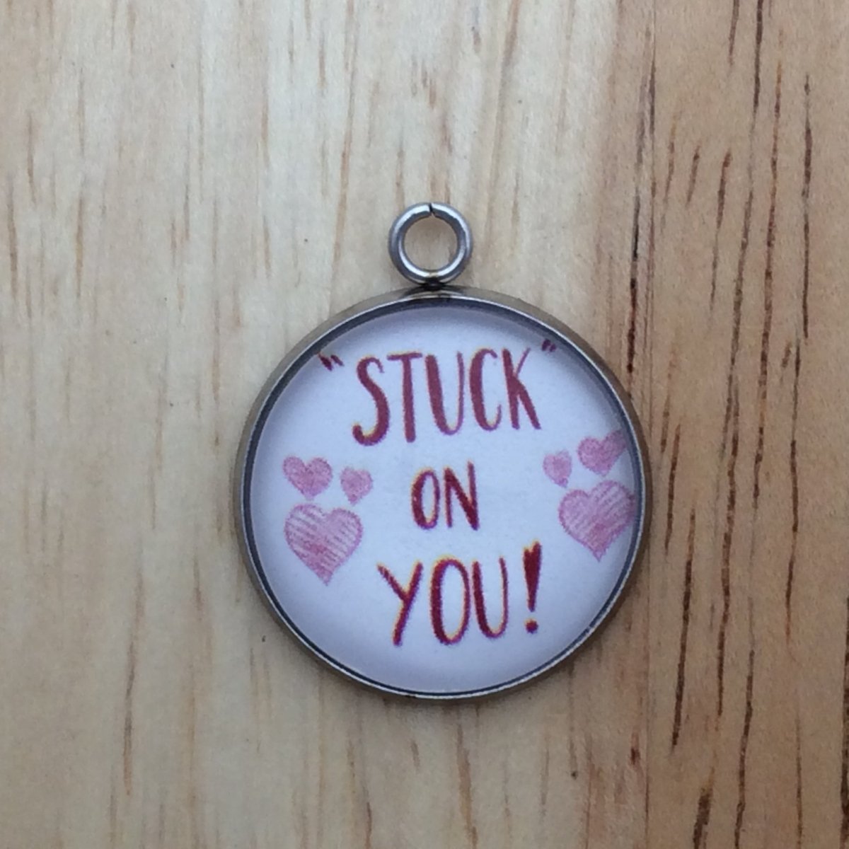 one glass cabochon charm with pink hearts and in red says stuck on you