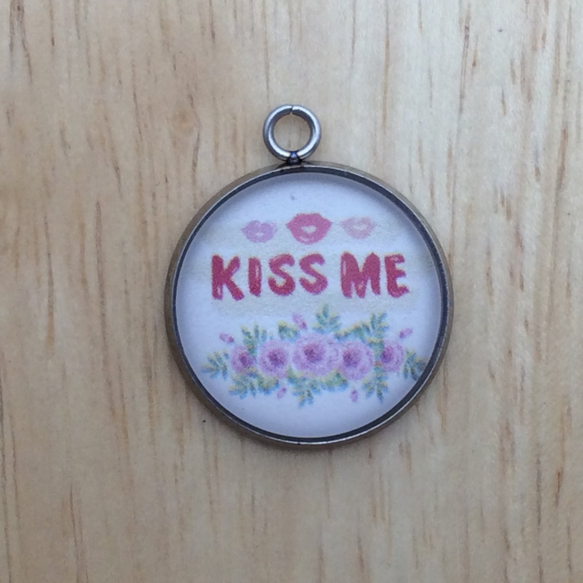 one glass cabochon charm with pink lips that says kiss me in red over pink flowers