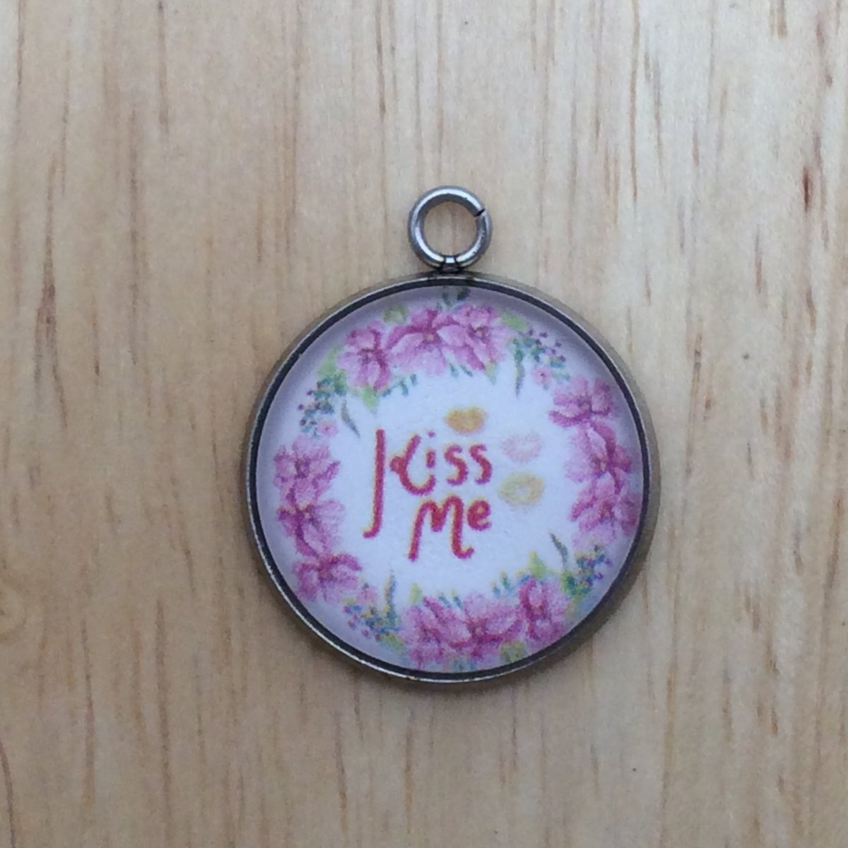 one glass cabochon charm with a floral wreath that says kiss me inside.